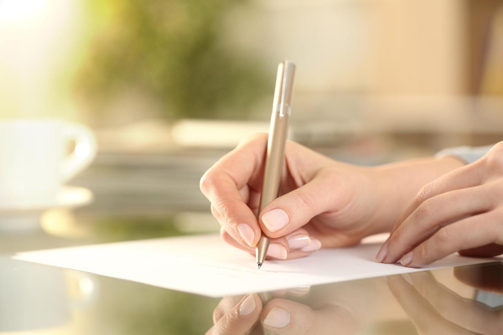 Mani di una donna che scrive un documento su una scrivania, riferimento alla consulenza tecnica